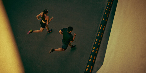 Fit young couple runs side by side along an urban route with powerful momentum. Outdoor training,...
