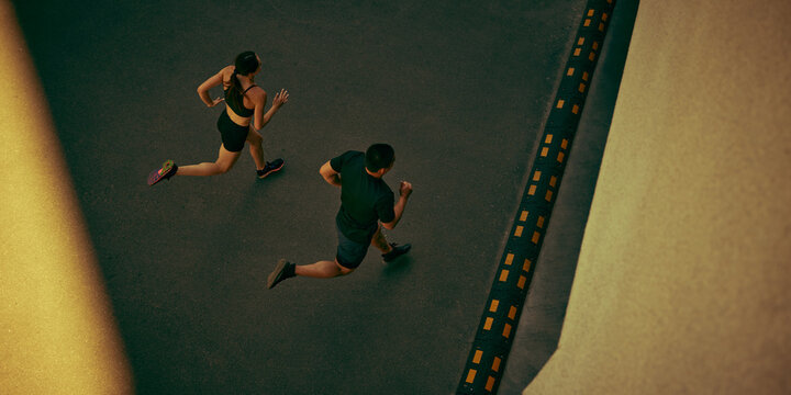 Fit young couple runs side by side along an urban route with powerful momentum. Outdoor training, cardiovascular health and shared goals concept.