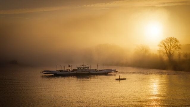 Aerial view of a ferry crossing the river during a foggy sunrise in Beesel, Limburg, Netherlands.