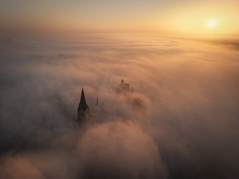 Aerial view of a church spire emerging from a thick layer of morning fog during sunrise in Kessel, Limburg, Netherlands.