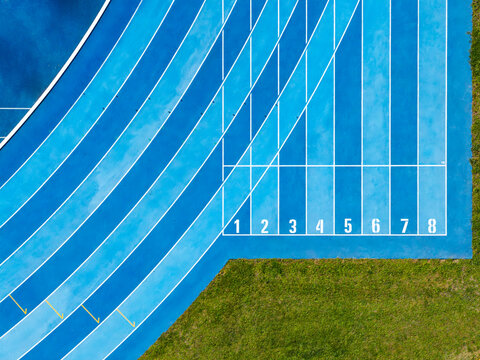 Aerial view of a blue running track with lanes numbered one to eight and green grass borders in Poland.