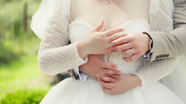 A couple stands close together on their wedding day. They hold each other gently. The setting has trees and grass in the background.