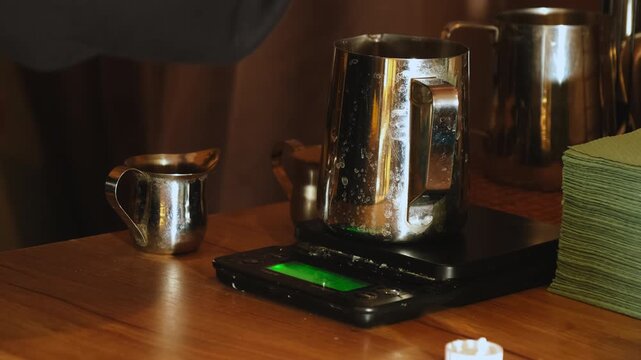Bartender hand pours syrup into stainless jug on digital scale closeup. Barkeeper makes coffee cocktail using tasty ingredients in coffeeshop