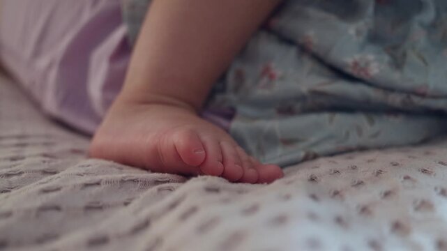 Close up of a baby foot resting on a soft textured blanket in a cozy bedroom setting at home