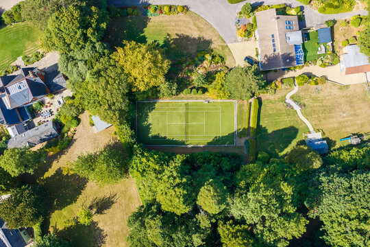 Aerial view of a private tennis court nestled within lush green gardens and mature trees in a residential area of Cheltenham, England, United Kingdom.