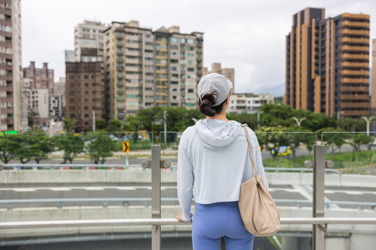 Woman leaning on bridge railing looking at city