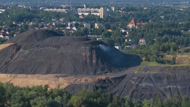 Smoking coal slag heap releasing pollution into the air near a city in silesia