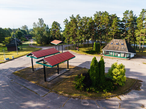 Aerial view of an abandoned former gas station with red roofs surrounded by pine trees in Platene, Ventspils novads, Latvia.