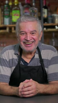 Senior bistro proprietor resting elbows on register counter while chuckling warmly expressing cheerful approachability lighthearted hospitality and casual local charm