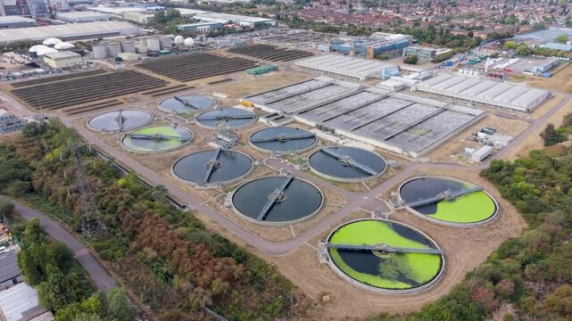Thames Water Edmonton treatment works seen from drone as it orbits above circular clarifiers and basins. Bright green algae blooms stand out in the first round tank system, North London.