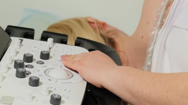 Cardiologist adjusts ultrasound controls during heart examination. Physician fine-tunes precise settings and observes patient on bed