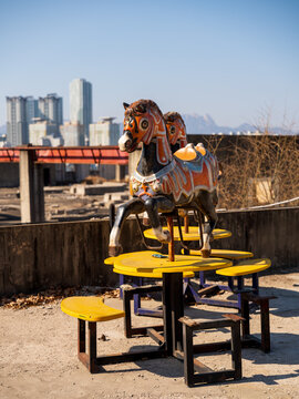 View of a vintage carousel horse mounted on a yellow table at the abandoned Yongma Land amusement park with the city skyline in the background in Seoul, Seoul, South Korea.