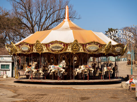View of the vintage carousel at the abandoned Yongma Land amusement park, featuring ornate golden details and painted horses under a clear blue sky in Seoul, Seoul, South Korea.