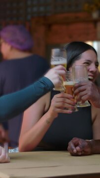 Young woman laughing heartily with friends over draft beer glasses at restaurant table for cheerful socializing weekend happiness and authentic friendship connection
