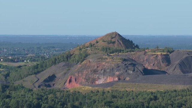 Aerial view flying towards a mining spoil tip landscape in a green forest area