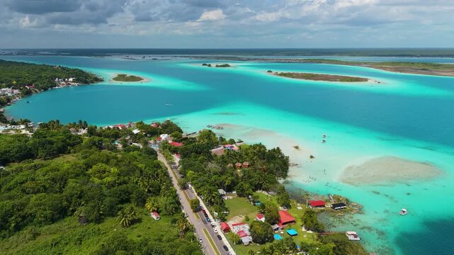 A winding coastal road and lush tropical vegetation border shallow aquatic shoals.