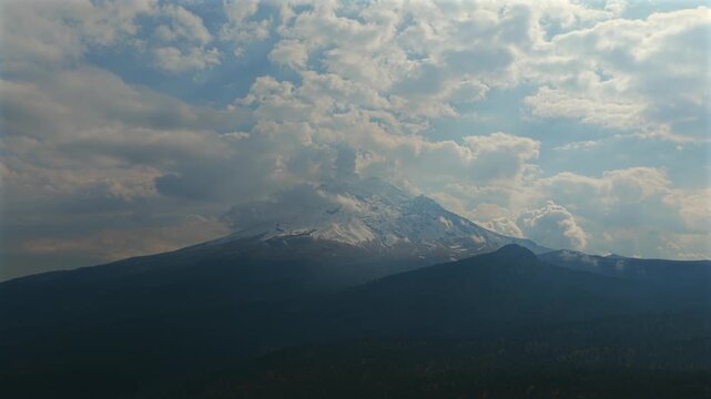 Snow covered Popocatepetl beneath cloudscape in Izta Popo Zoquiapan National Park, Mexico. Establishing shot.