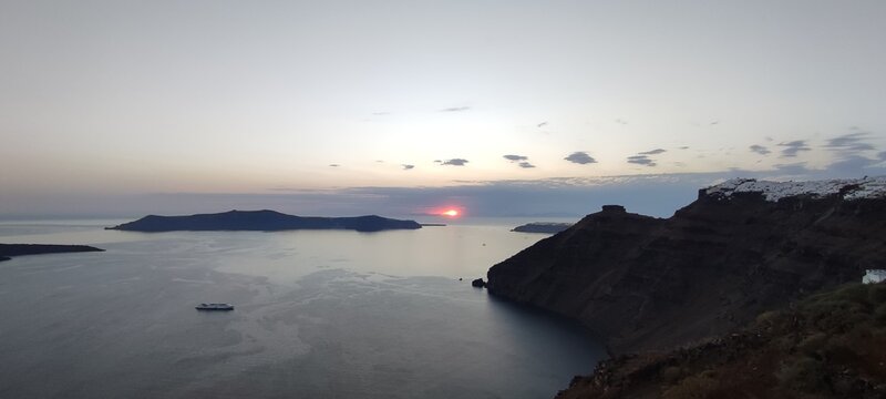 Sunset view of the Santorini caldera with volcanic islands and calm Aegean Sea under warm evening light. A serene Mediterranean landscape ideal for travel, tourism, nature, and destination concepts.
