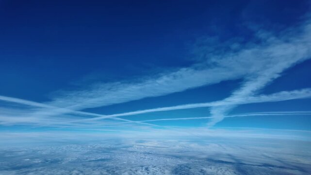 Cockpit view in a stratospheric flight with the view of multiple jet contrails in a deep blue sky, flying well above an endless layer of clouds. 4K