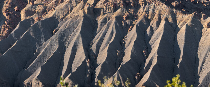View of the rugged, eroded slopes and dramatic ridges of Factory Butte, showcasing the stark geological formations and desert landscape in Wayne County, Utah, United States.