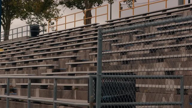 Static view of empty concrete bleachers seen through a chain-link fence outdoors.