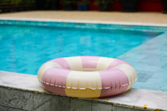 Pink inflatable ring floating beside swimming pool with turquoise water and tiled edge, creating playful summer leisure scene with gentle relaxation and outdoor recreation mood