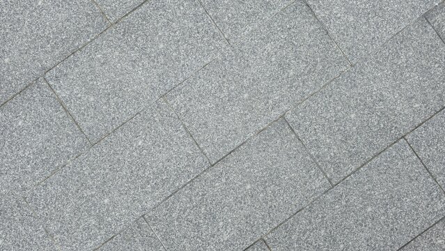 Grey granite stone flooring with diagonal brick pattern. Diagonal grey granite blocks pavement backdrop texture. Top view of rectangular grey granite tiles laid diagonally on outdoor pavement.