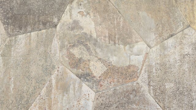 Natural stone wall texture with orange and grey stones. Vintage rustic stone wall background with dark stains. Close-up of a rustic stone cladding wall showing organic polygonal shapes.
