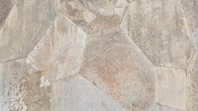 Natural stone wall texture with orange and grey stones. Vintage rustic stone wall background with dark stains. Close-up of a rustic stone cladding wall showing organic polygonal shapes.