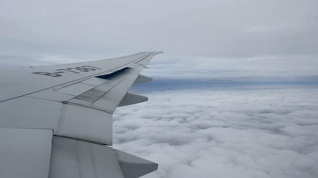 View from an airplane window showing the wing above a vast layer of white clouds. Overcast skies stretch across the horizon during flight over Russia.