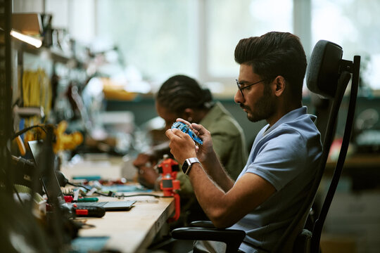 Side view of young Indian male engineer examining circuit board in electronics workshop. Suitable for hardware engineering, technical research, STEM education campaigns