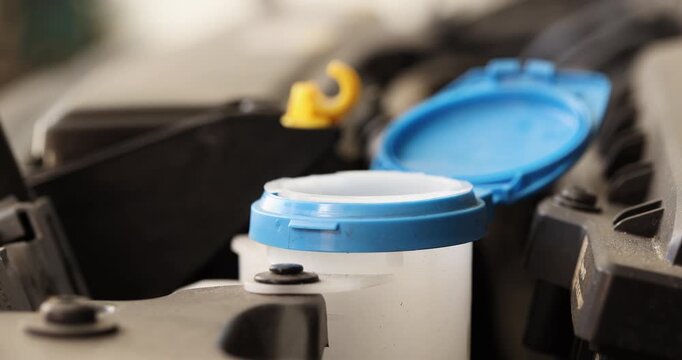 Close-up view of windshield washer fluid being poured into the washer reservoir of a modern vehicle during the engine routine maintenance.