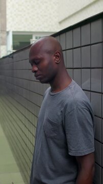Pensive African American individual leaning shoulder against tiled domestic wall with bowed head confronting unresolved dilemmas quiet doubt and heavy memories