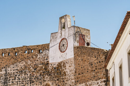 View of the historic stone clock tower and fortification wall under a clear blue sky in Sines, Setubal, Portugal.