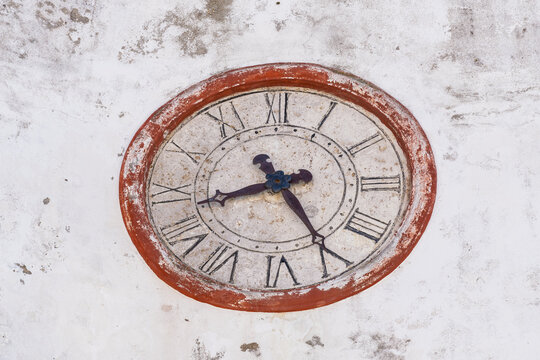 View of an antique circular clock with Roman numerals mounted on a weathered white stone wall in Sines, Setubal, Portugal.