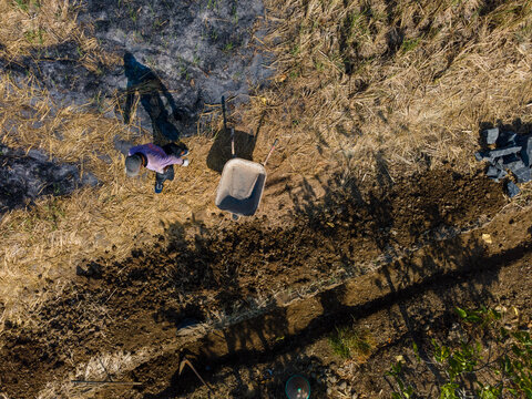 Aerial View of a Farmer with a Traditional Farm Cart in an After-Harvest Rice Field Covered with Rice Straw Ash. Farming Activity, Agricultural Labor, and Post-Harvest Field Management from Above.