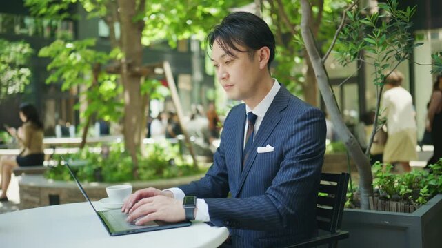 Japanese businessman working on a laptop at an outdoor cafe