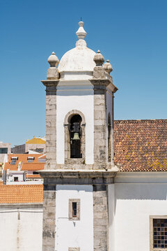 View of the historic church bell tower with stone detailing and a terracotta roof against a clear blue sky in Sines, Setubal, Portugal.