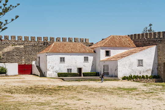 View of the historic Castle of Sines with its white walls, orange tiled roofs, and stone battlements under a clear blue sky in Sines, Setubal, Portugal.