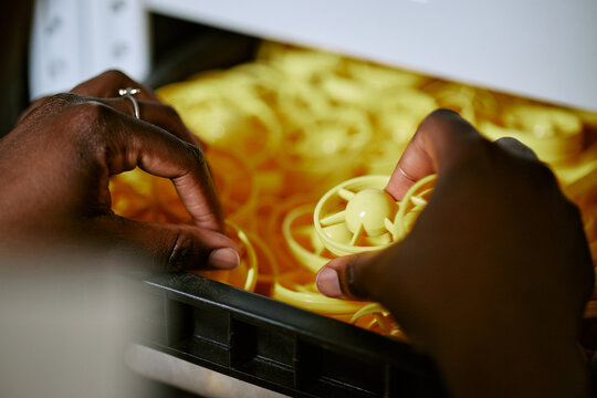 Close up of African American woman hands selecting plastic components from storage bin in manufacturing warehouse. Industrial image suitable for assembly line and supply chain marketing