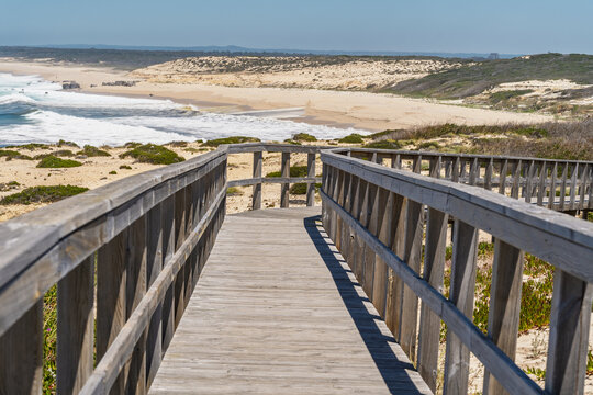 View of a wooden boardwalk leading to the sandy beach and dunes at Praia da Lagoa de Albufeira in Sesimbra, Setubal, Portugal.