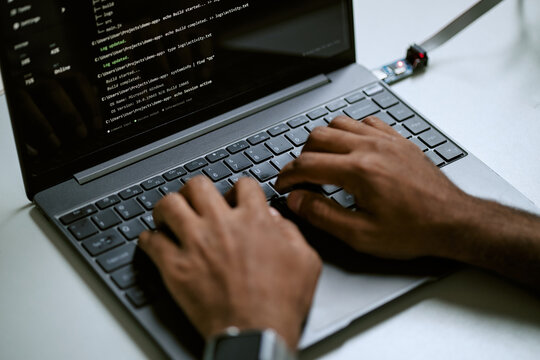 High angle closeup of African American programmer typing code on laptop keyboard. Visual metaphor for software development, programming education, cyber security, data science