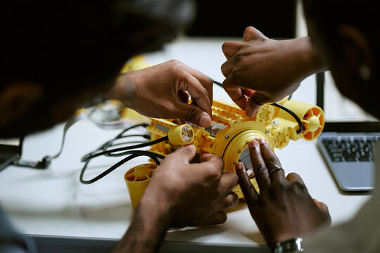 Diverse young engineering students assembling yellow underwater drone prototype in robotics laboratory. Image suitable for STEM education, technology research, innovation marketing