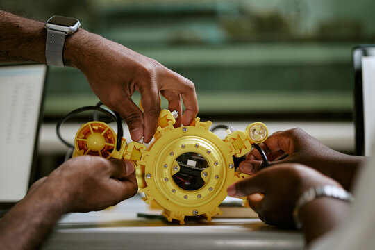 African American engineers assembling yellow robotic underwater drone prototype in tech laboratory. Useful for STEM education and robotics engineering campaign