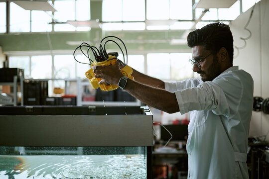 Young Indian male engineer testing robotic underwater device above water tank in laboratory. Useful for marine robotics technology, scientific research and engineering education