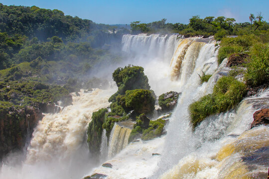 View of Iguazu Falls with cascading water, lush green vegetation on rocky cliffs, and mist rising in Foz do Iguacu, Parana, Brazil.