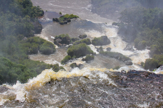 View of the powerful cascading waters of Iguazu Falls surrounded by lush green vegetation and rocky outcrops in Foz do Iguacu, Parana, Brazil.