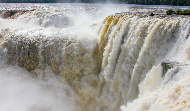 View of the powerful cascading waters of Iguazu Falls with mist rising from the river, surrounded by lush tropical vegetation in Foz do Iguacu, Parana, Brazil.