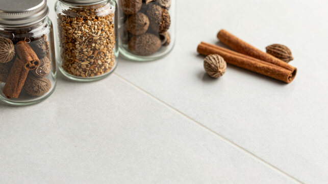 Glass jars filled with spices, cinnamon sticks, and nutmeg on a white tiled surface