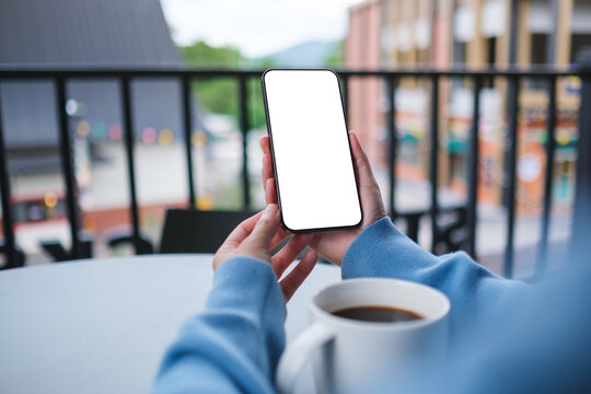 Mockup image of a woman holding and using mobile phone with blank desktop screen in cafe